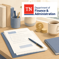 Desk with a grant application form, pen, notebook, coffee mug, stacked coins, and a Tennessee Department of Finance and Administration logo displayed in the background.